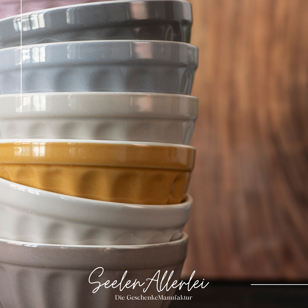 verschiedenfarbige Schalen aus Steingut von mynte IB Laursen übereinandergestapelt vor einer Holzwand