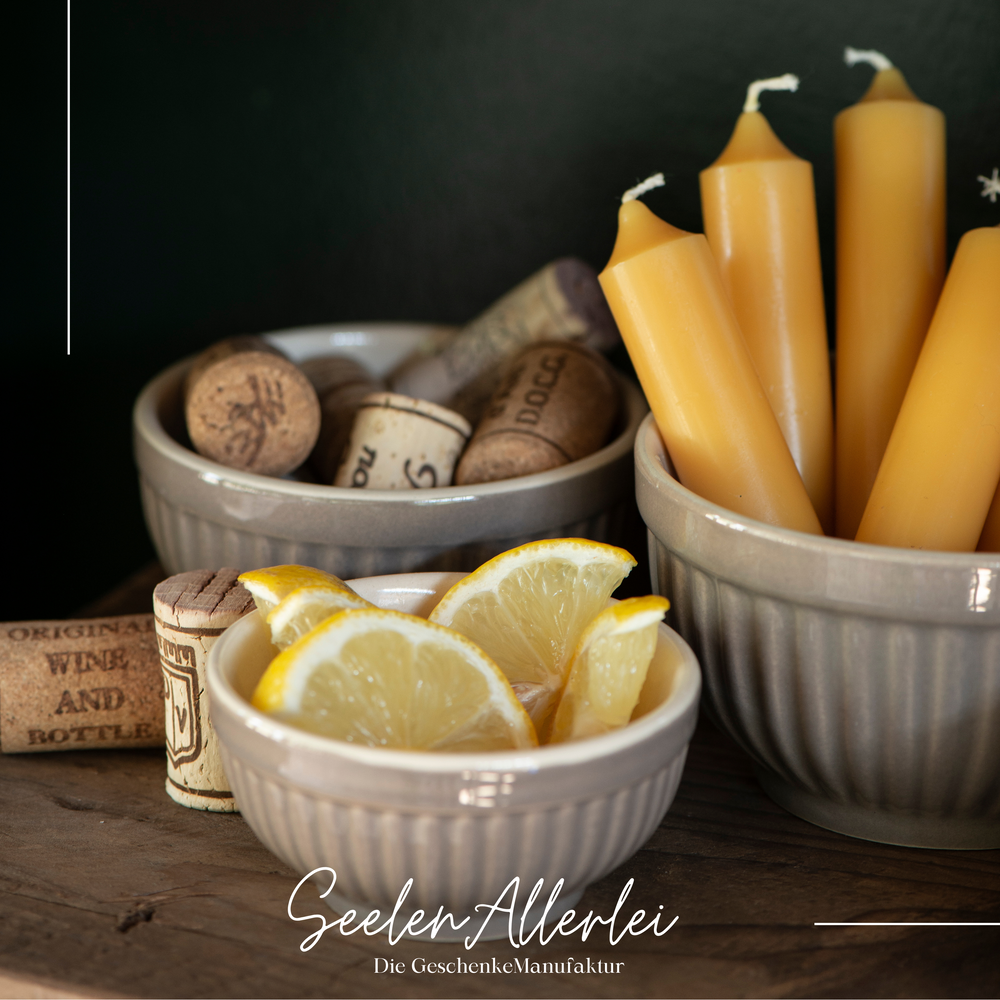 drei verschieden große Schalen mit Rillendesing gefüllt mit Kerzen, Korken und Zitronenscheiben auf einem Holzregal