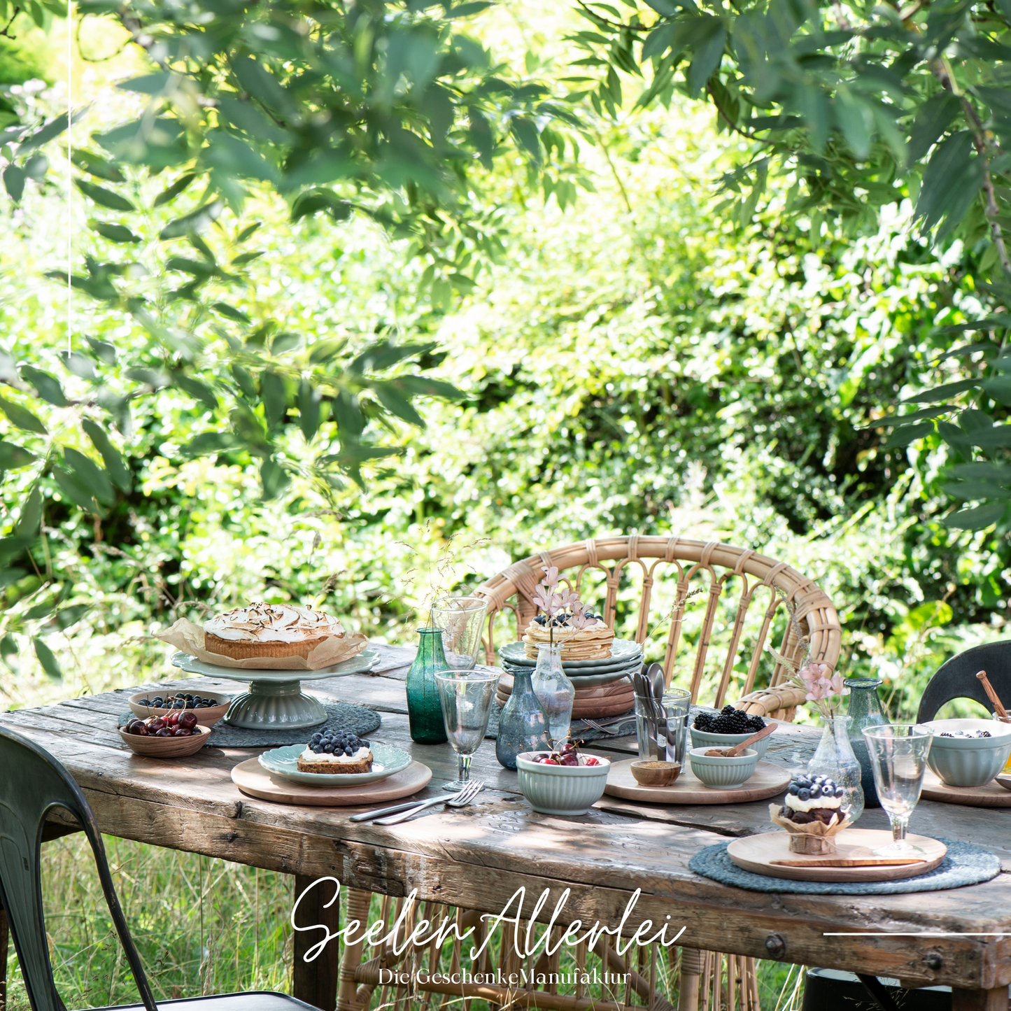 schön gedeckter Holztisch im gut bewachsenen Garten geschmückt mit Kuchen und Schalen, Gläsern und schönen Gedecken zum Feiern und genießen