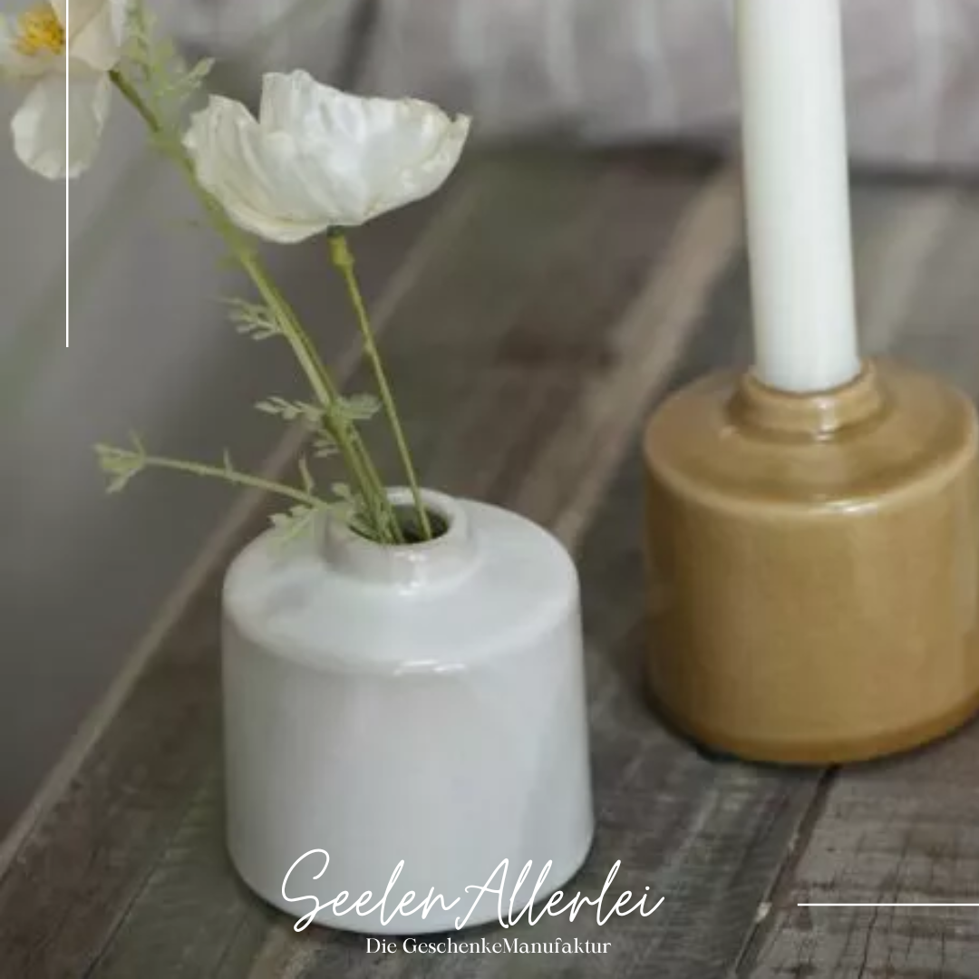 zwei verschiedenfarbige Vasen, einmal als Vase mit Blume und einmal umgewandelt als Kerzenhalter mit einer weißen Kerze stehen auf einem Holztisch zur Dekoration