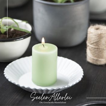 Kerzenteller aus Emaille steht mit einer angezündeten Kerze auf einem Holztisch zusammen dekoriert mit einer Topfblume und Juteband
