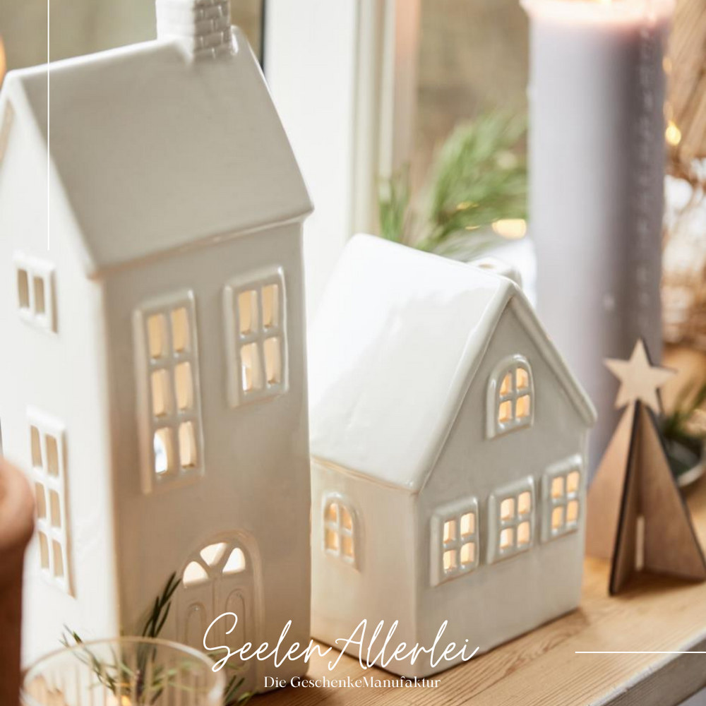 Weiße Keramikhäuser Kollektion für Teelichter beleuchtet auf Regal als gemütliche Hygge Dekoration