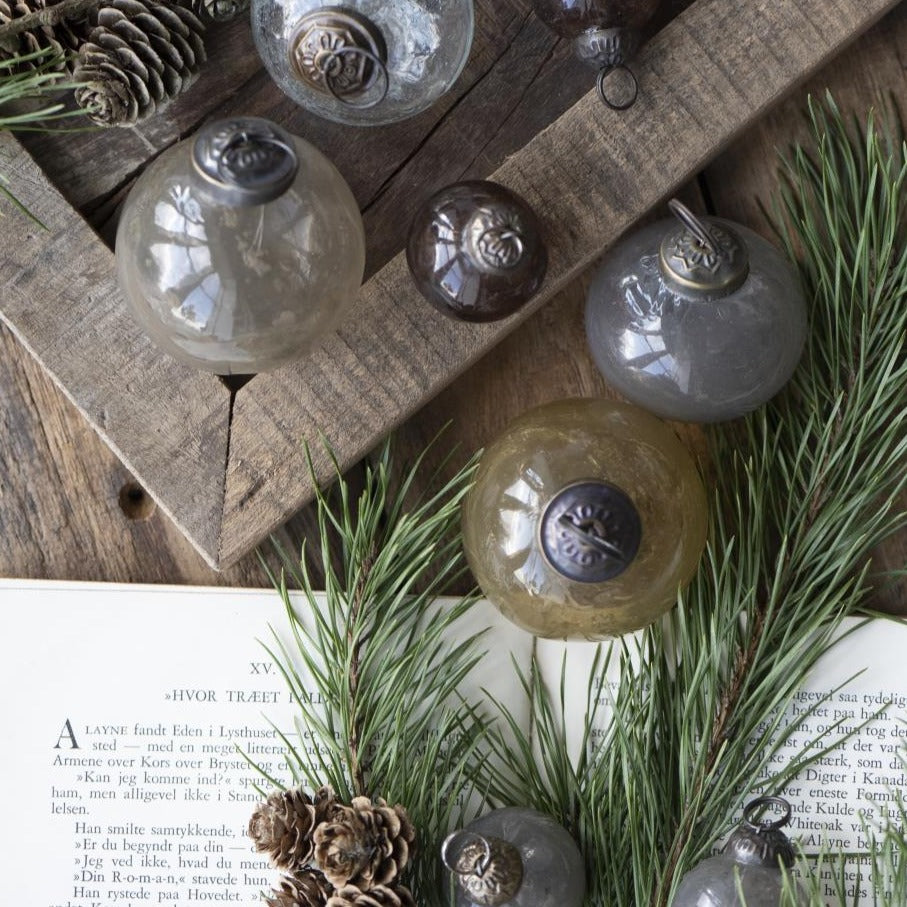 mehrere Glaskugeln liegen auf einem Holztisch mit einem aufgeschlagenen Buch und Tannenzweigen