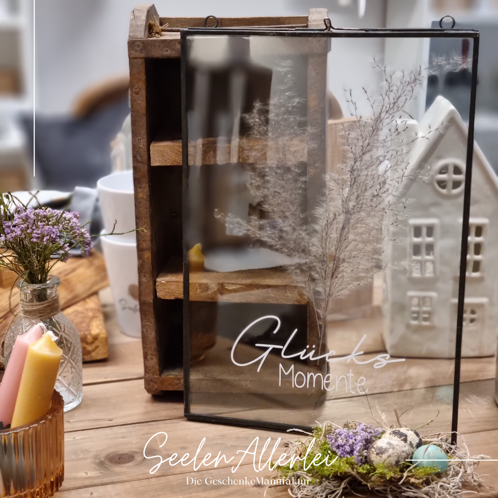 stehender Glasrahmen in schwarz mit Trockenblumendekoration vor einer Ziegelform von Iblaursen