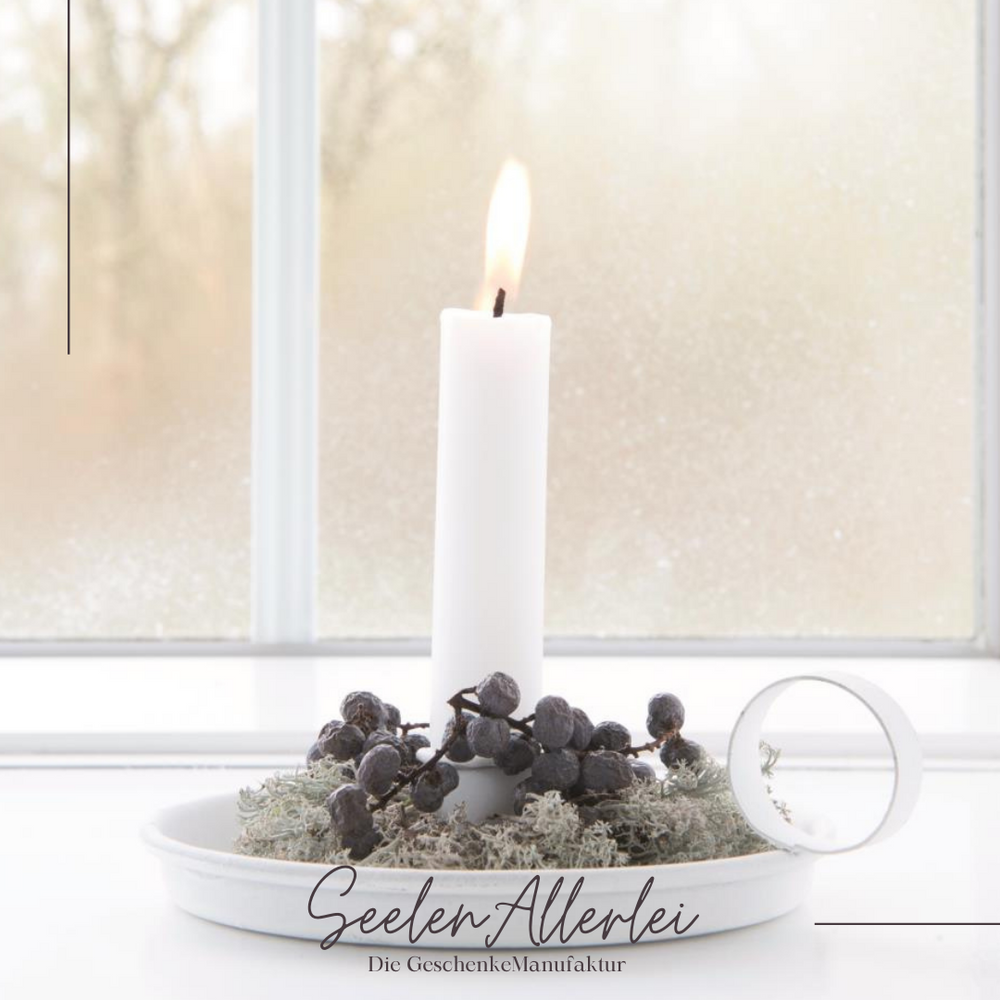 dekorierte Kammerleuchte in weiß mit einer brennenden weißen Kerze vor einem Fenster auf der Fensterbank